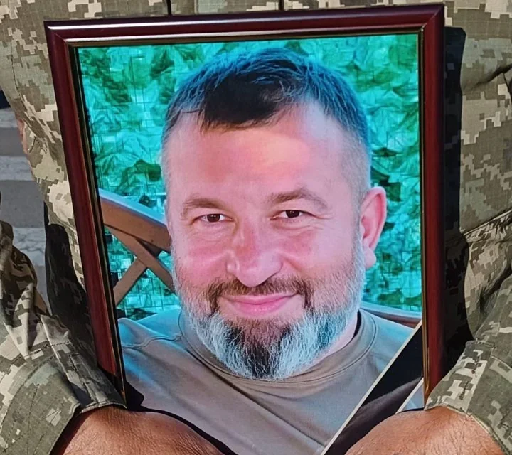 Військовий у піксельному камуфляжі тримає рамку з портретом усміхненого бородатого чоловіка