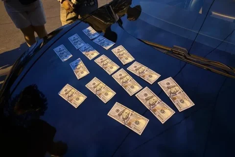 Стодоларові купюри розкладені на блискучому капоті темного автомобіля