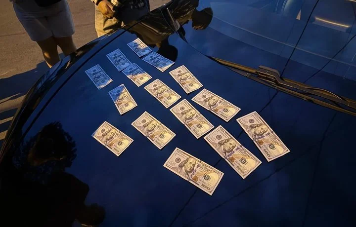 Стодоларові купюри розкладені на блискучому капоті темного автомобіля